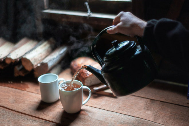 Person pouring a cup of tea from a black teapot.